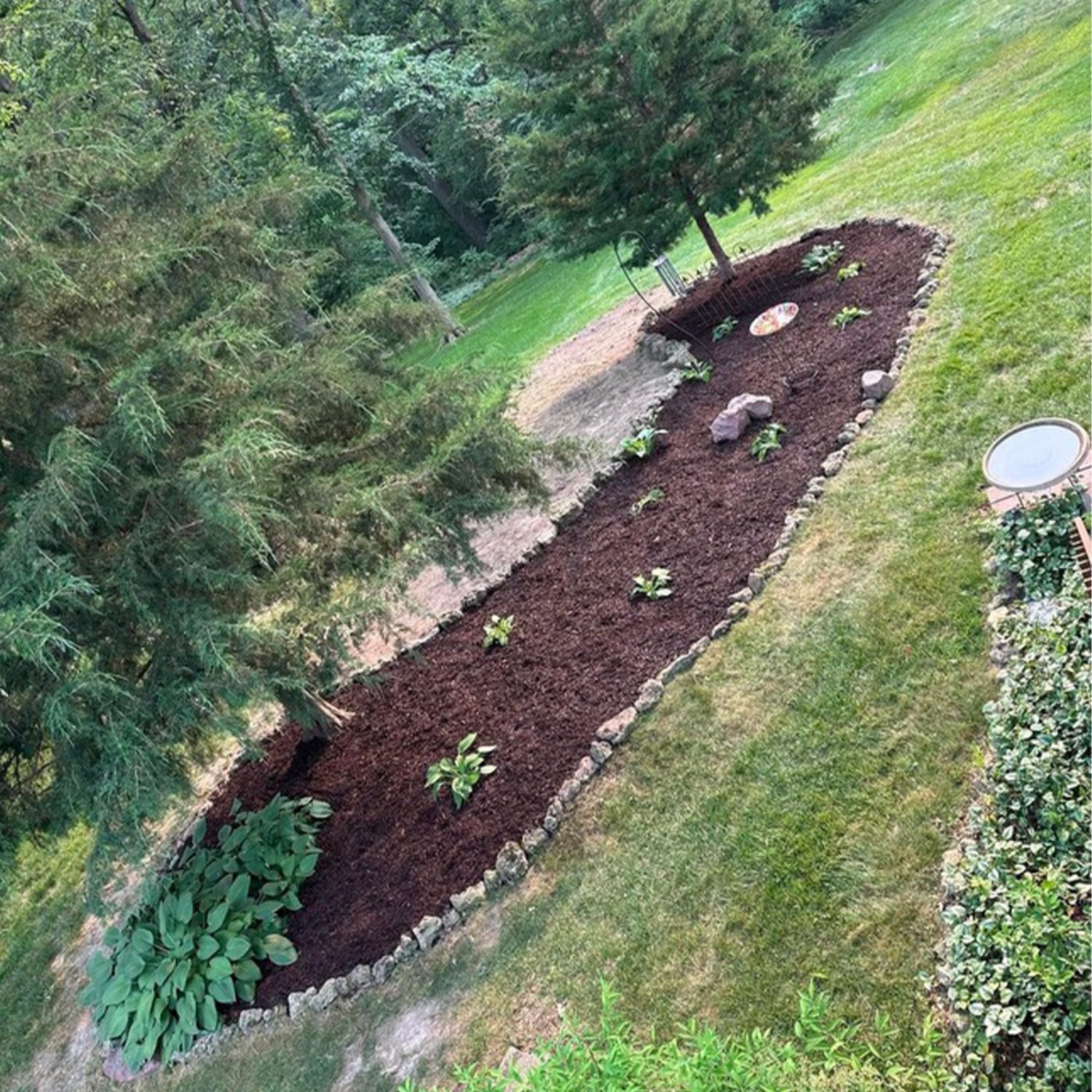 An image of a large garden landscaping project with healthy plants, rock edging, mulch, and garden ornaments.