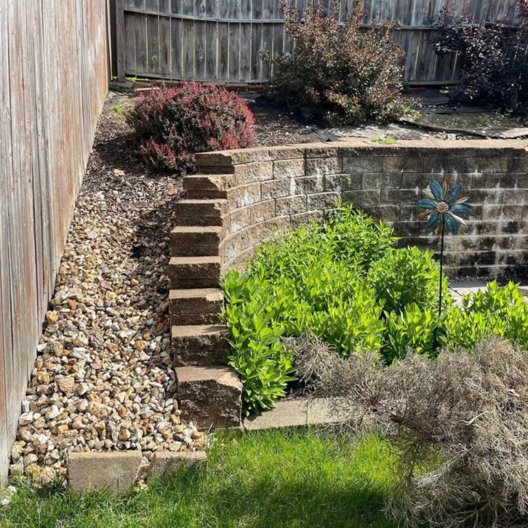 The before image of a landscaping project showing rock and exposed landscape fabric in a garden above a retention wall.