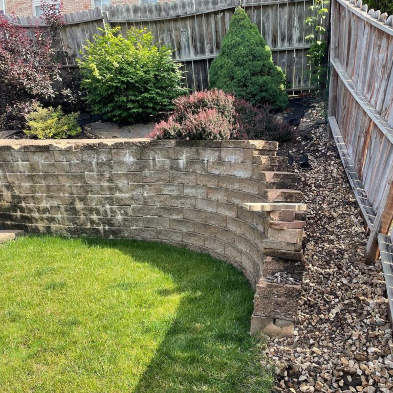 The before image of a landscaping project showing rock and exposed landscape fabric in a garden above a retention wall.